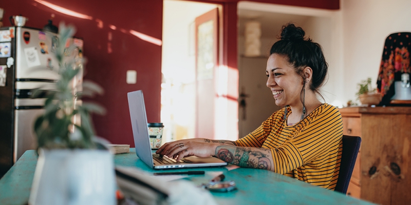 woman sitting at kitchen table smiling and using a laptop