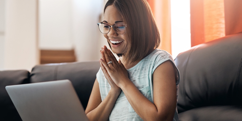 woman on couch smiling as she looks at her laptop